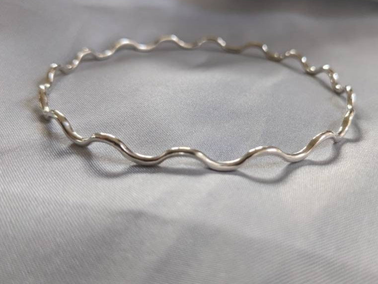 A sterling silver wavy bangle bracelet displayed on a grey surface.