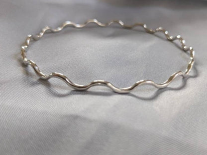 A sterling silver wavy bangle bracelet displayed on a grey surface.