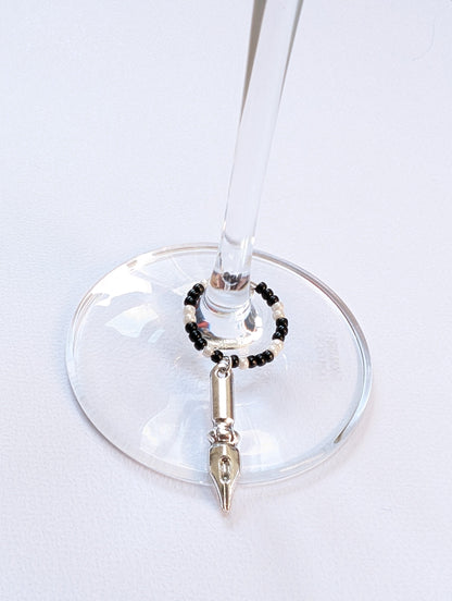 Close-up of a wine glass with a decorative 'black pen' charm on a white surface