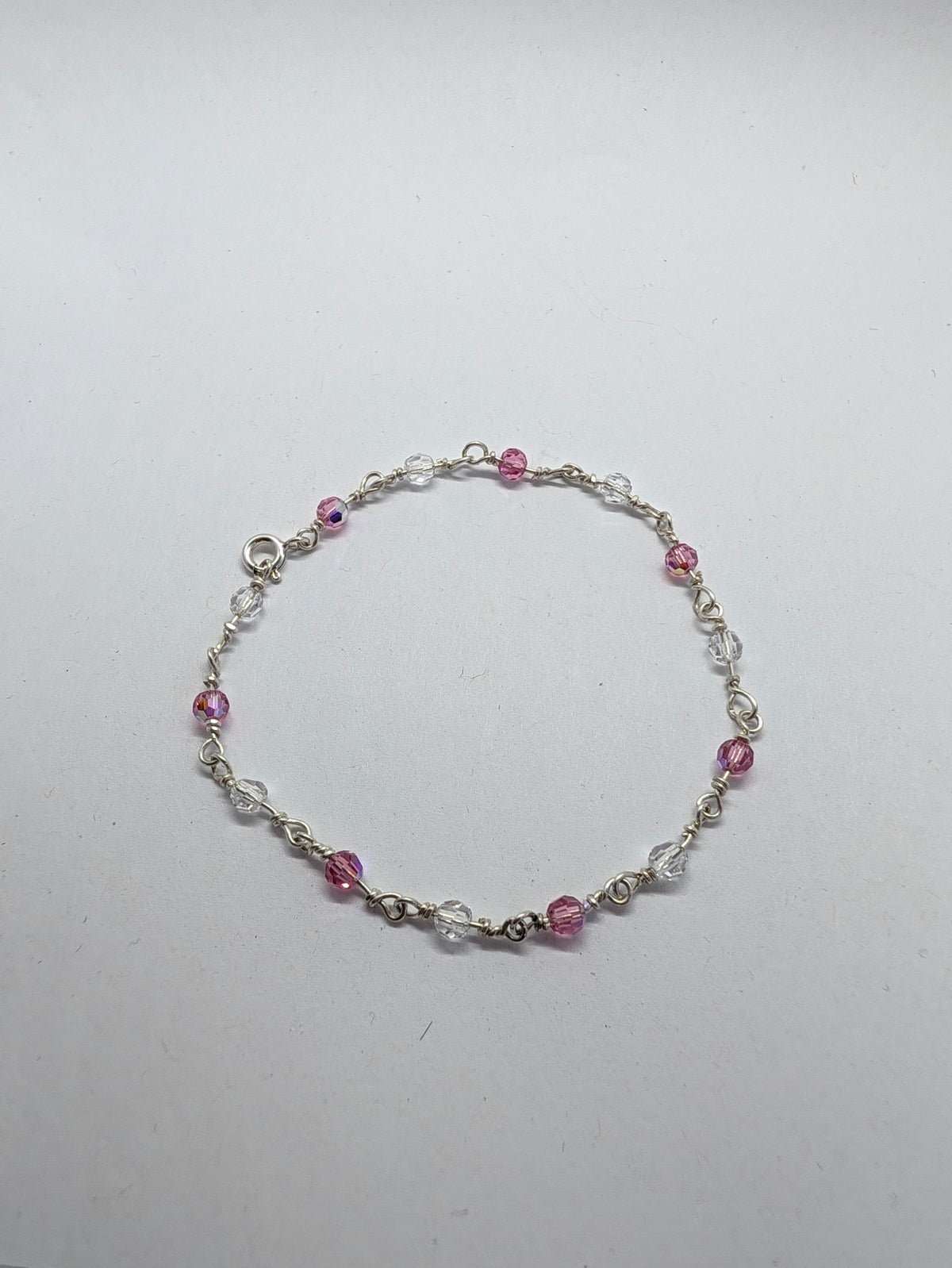 A delicate sterling silver beaded bracelet with alternating pink faceted beads and clear crystal beads, displayed on a plain light gray background.

