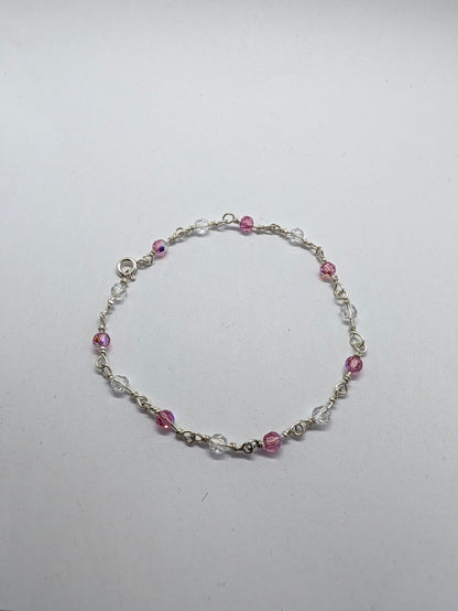 A delicate sterling silver beaded bracelet with alternating pink faceted beads and clear crystal beads, displayed on a plain light gray background.

