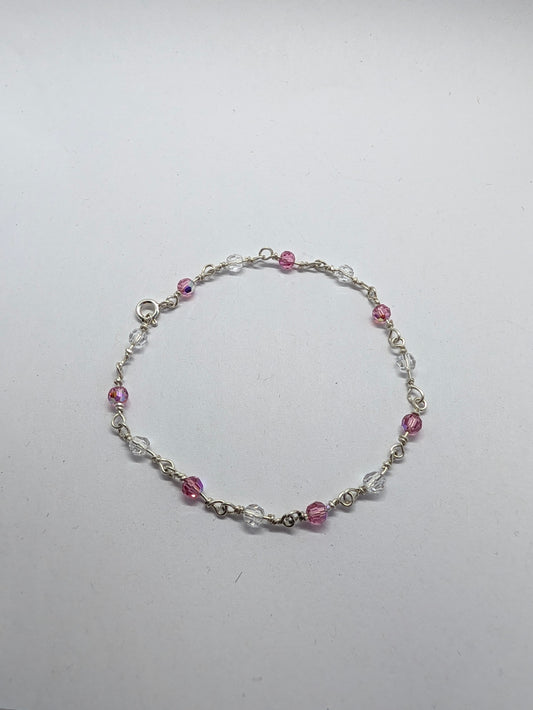 A delicate sterling silver beaded bracelet with alternating pink faceted beads and clear crystal beads, displayed on a plain light gray background.

